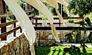 Dekorativa tygstycken svajar i vinden på en terrass med stenmur och blommor. (AI-genererad text)