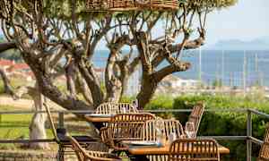 Uteservering med rottingstolar och utsikt över havet. (AI-genererad text)