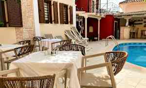 Bord och stolar vid en pool utomhus, omgiven av byggnader med fönsterluckor. (AI-genererad text)