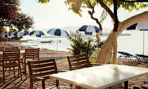 Utemöbler med stolar och bord nära en strand med parasoller. (AI-genererad text)