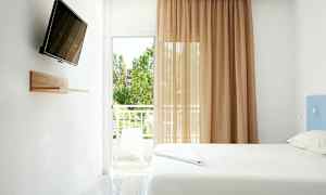 Ett ljust rum med en säng, en väggmonterad TV, och en balkong med utsikt. (AI-genererad text)