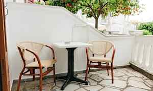 En liten uteplats med två stolar och ett bord framför ett apelsinträd. (AI-genererad text)