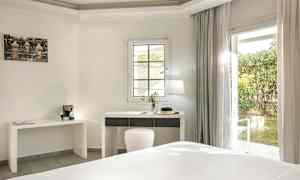 Ett ljust hotellrum med ett skrivbord och en fönsterdörr ut mot en trädgård. (AI-genererad text)