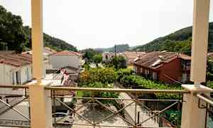Vy från en balkong över hus med tegeltak och grönska samt berg i bakgrunden. (AI-genererad text)