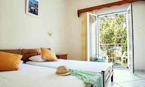 Ett hotellrum med enkelsängar, öppet fönster och utsikt mot balkong. (AI-genererad text)