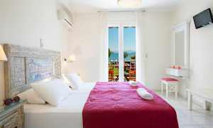 Ett ljus och luftigt hotellrum med en dubbelsäng utrustad med vitt linnet och en lila quilt. Fönster med utsikt mot havet och en balkong. (AI-genererad text)