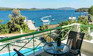 Utsikt från en balkong mot en blå havsvik med båtar och grönskande omgivningar. (AI-genererad text)