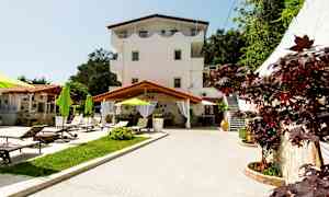 Utomhus miljö med en byggnad i tre våningar, solstolar och gröna parasoller. (AI-genererad text)