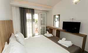 Ett hotellrum med en dubbelsäng, en TV på en träbänk, och en balkong med utsikt. (AI-genererad text)