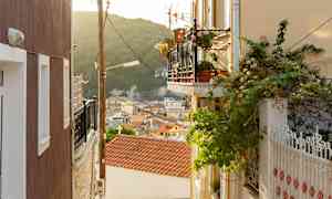 En gränd med balkonger och växtlighet, utsikt över hustak och trädklädda berg. (AI-genererad text)