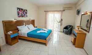 Ett hotellrum med en dubbelsäng, målning ovanför sängen, och glasdörrar som leder till en balkong. (AI-genererad text)