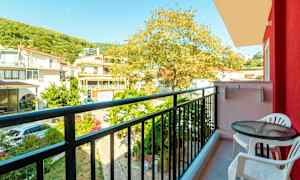 En utsikt från en balkong med ett bord och två stolar samt omgivande byggnader och träd. (AI-genererad text)