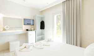 Ett hotellrum med en bäddad säng, TV, kylskåp och garderob. (AI-genererad text)