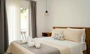 Interiör av ett sovrum med en bäddad säng, tre hoprullade handdukar och en balkongdörr med gardiner. (AI-genererad text)