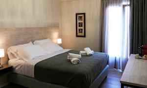 Hotellrum med en dubbelsäng, sängbord med lampor, hoprullade handdukar på sängen och ett fönster med gardiner. (AI-genererad text)