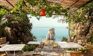 Omgivning med utsikt mot havet, bord och stolar på en veranda med gröna växter. (AI-genererad text)