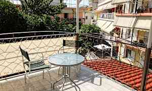 Balkong med glasbord och två metallstolar, med utsikt över grönska och omgivande byggnader. (AI-genererad text)