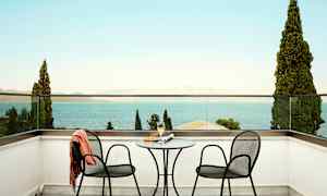 Två stolar och ett bord på en terrass med utsikt över havet. (AI-genererad text)