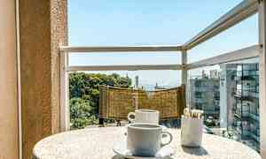 En balkong med utsikt över havet. På bordet finns två kaffekoppar och en behållare med sockersticks. (AI-genererad text)