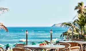 Utsikt över bord med drinkar och frukt mot havet. (AI-genererad text)