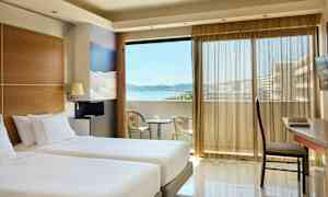 Rum med två enkelsängar, en balkong med utsikt över havet och sittmöbler. (AI-genererad text)