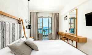 Ett ljust och modernt inrett hotellrum med säng och utsikt mot havet från en balkong. (AI-genererad text)