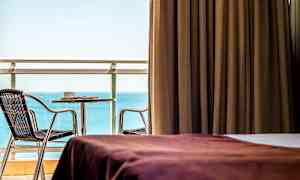 Rum med brun gardin, utsikt mot havet samt möblerad balkong. (AI-genererad text)
