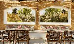 En uteplats med sittplatser och bord, stenmur och stora fönster med utsikt över grönska. (AI-genererad text)