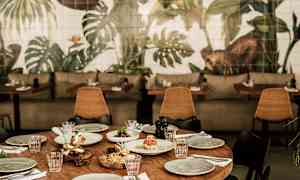 En dukad träbord omgiven av stolar, med en bakgrund av väggmålningar med växtmotiv. (AI-genererad text)