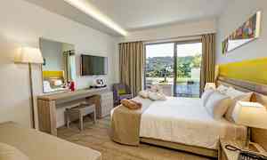 Ett hotellrum med säng, skrivbord, TV, och en balkong som visar en grön utsikt. (AI-genererad text)