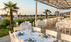 Uteservering med vita bord och stolar, palmträd och havsutsikt. (AI-genererad text)