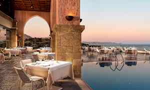 Uteservering med dukade bord bredvid en pool och havsutsikt vid solnedgång. (AI-genererad text)