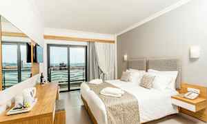 Ett hotellrum med en stor säng, ljusa möbler, och en balkong med utsikt. (AI-genererad text)