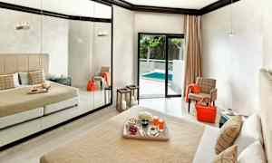 Ett hotellrum med en stor spegelvägg, en säng med beige överkast och kuddar, och en balkong dörr som leder ut till en pool. (AI-genererad text)