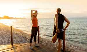 Två personer stretchar på en träbrygga vid en strand under solnedgången. (AI-genererad text)