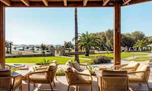 Avkopplingsområde med sittmöbler som leder till en trädgård med palmer och havsutsikt. (AI-genererad text)