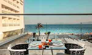 Utsikt från ett bord på en terrass med apelsinjuice och bakverk, mot havet och en palm. (AI-genererad text)