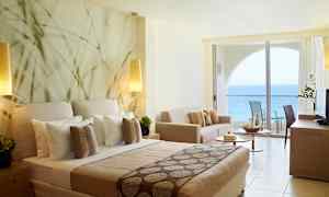 Hotellrum med havsutsikt och modern inredning inklusive säng, soffa och balkong. (AI-genererad text)