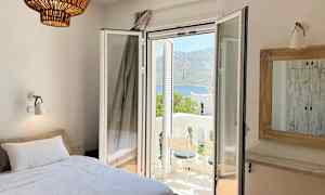 Rum med säng, öppen balkongdörr och utsikt över ett bergigt landskap. (AI-genererad text)