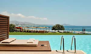 Vy från en pool med utsikt mot havet, solstolar och parasoller. (AI-genererad text)