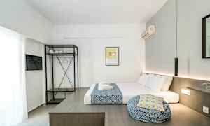 Ett modernt hotellrum med en säng bäddad med vita och blåfärgade textilier, en öppet garderob med hyllplan och klädhängare samt en väggmonterad luftkonditionering. (AI-genererad text)