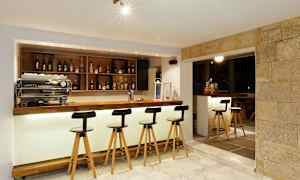 En modern bardisk med höga stolar, flaskor på hyllor och ljus belysning. (AI-genererad text)