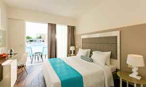 Ett hotellrum med en dubbelsäng, nattduksbord, en stol och ett skrivbord. Fönstret har utsikt över en pool. (AI-genererad text)