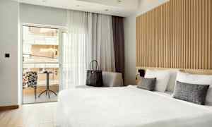 Bild av ett hotellrum med stort sängområde och en sittgrupp vid fönstret, som leder ut till balkongen. (AI-genererad text)