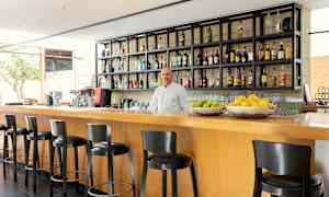 En modern bar med höga stolar vid en trädisk, hyllor fyllda med flaskor och fruktkorgar med citrusfrukter. (AI-genererad text)