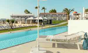 En solstol med en filt vid kanten av en pool, med en parasoll i förgrunden och hotellbyggnader i bakgrunden. (AI-genererad text)