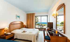 Ett hotellrum med två sängar, ett skrivbord, en spegel och en balkong med utsikt över havet. (AI-genererad text)