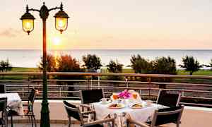 Utsikt över ett bord med frukostservering på en terrass med havet i bakgrunden. (AI-genererad text)