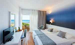 Hotellrum med två sängar och balkong med vy över havet. (AI-genererad text)