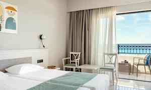 Hotellrum med dubbelsäng, två stolar och ett bord vid fönster med havsutsikt. (AI-genererad text)